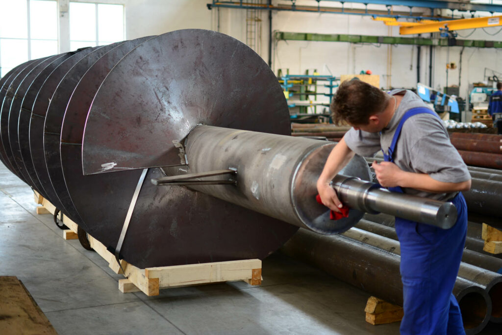 Worker polishing a helix rotor shaft designed for pulp and paper processing machinery