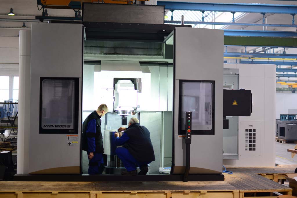 Two operators setting up the OKUMA VTM-1200YB vertical machining center for production